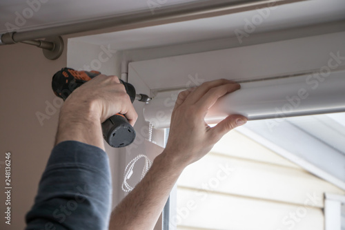 worker mounts roller blinds on window frames