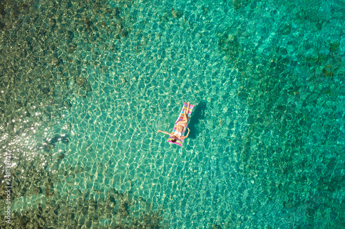 Top down view of a beautiful woman in a white bikini who is floating on a air mattress