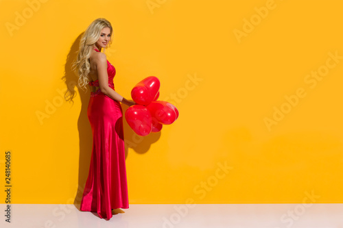 Beautiful Woman In Elegant Red Dress Is Posing With Heart Shaped Balloons