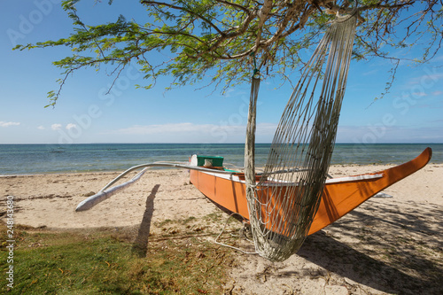 blue sea and fisher boat on a natural white beach and a hammock tied on a single tree 