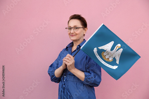 Louisiana flag. Woman holding Louisiana state flag. Nice portrait of middle aged lady 40 50 years old holding a large state flag over pink wall background on the street outdoor. photo