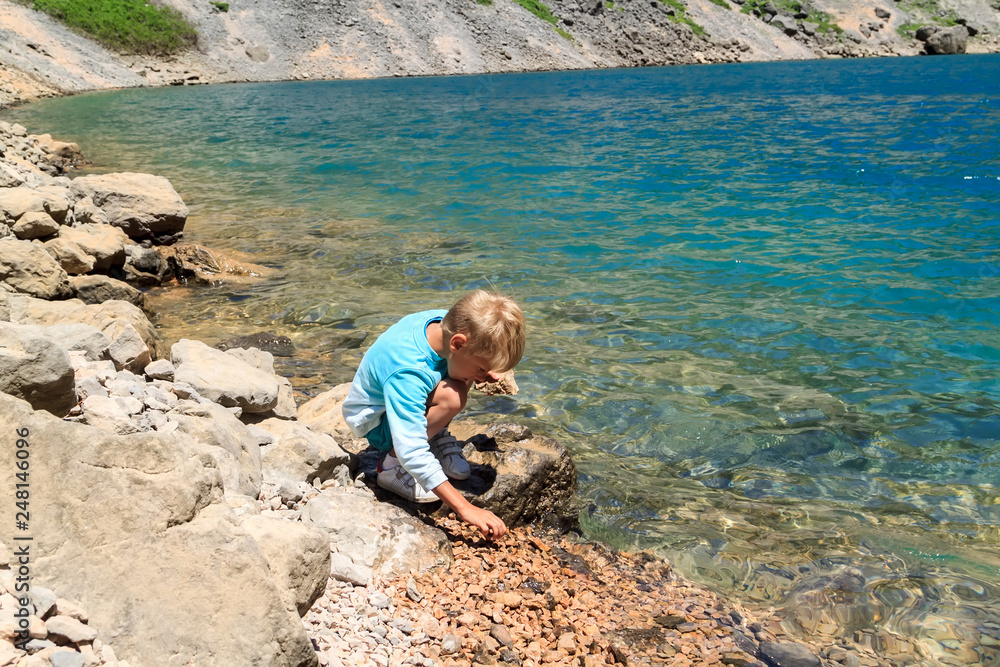 boy sits on the shore of the blue karst lake in the mountains