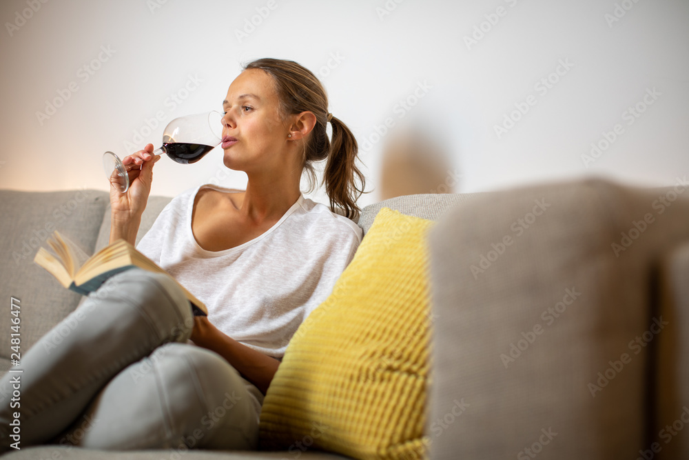 Pretty, young woman drinking some nice red wine at home, in the evening after work on her sofa (color toned image; shallow DOF)