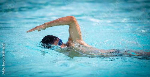 Man swimmer swimming crawl in a blue water pool. Portrait of an athletic young male triathlete swimming crawl wearing swimming goggles. Triathlete training for triathlon.