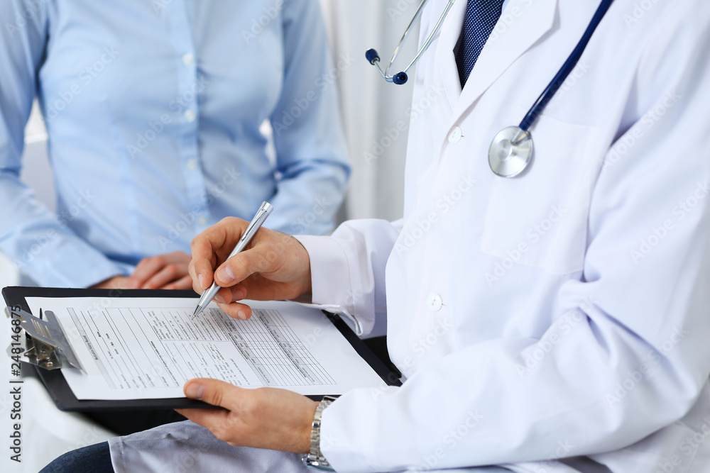 Male doctor holding application form while consulting female patient in hospital. Medicine and healthcare concept Male doctor holding application form while consulting female patient in hospital. Medicine and healthcare concept