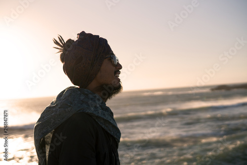 Young Asian Bearded Tourist man with Dreadlocks and scarf on head Walking on the Ocean Coast in Essaouira, Morocco at the evening sunset time