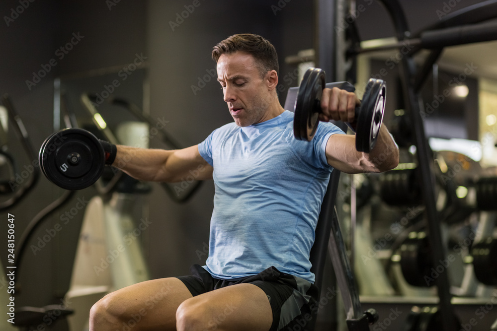 Muscular man doing exercise with dumbbell at the gym. Muscular man doing exercise with dumbbell at the gym.