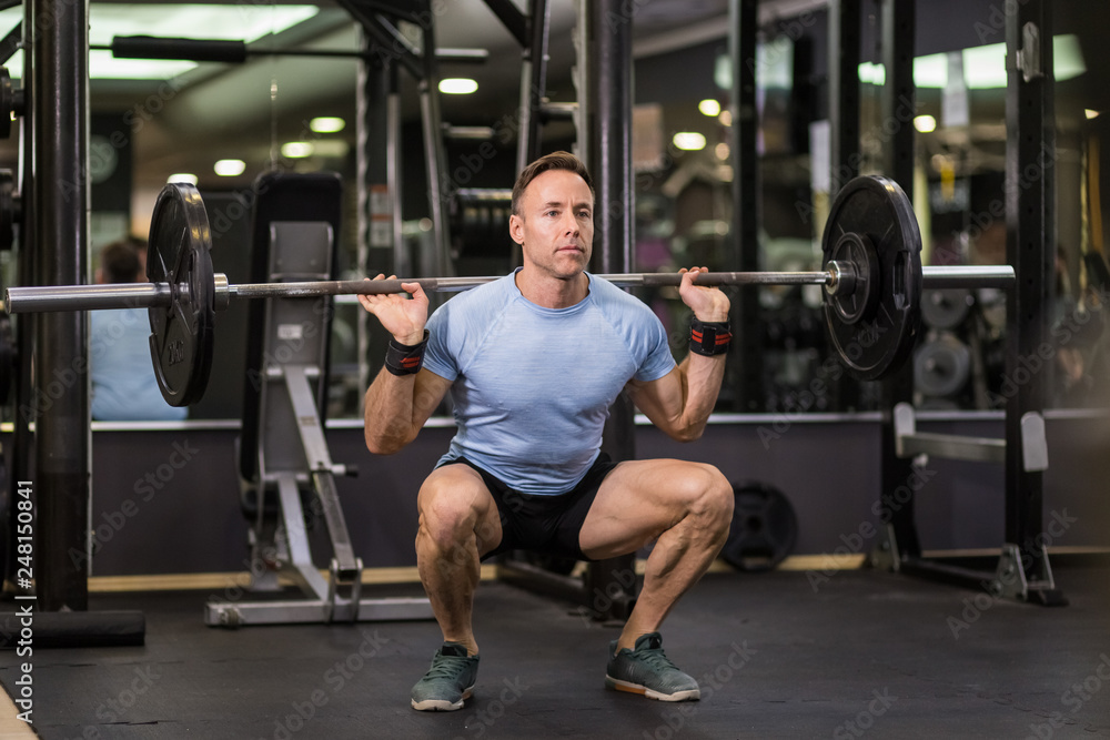 Image of a muscular man doing squads with heavy barbell at the gym. Image of a muscular man doing squads with heavy barbell at the gym.