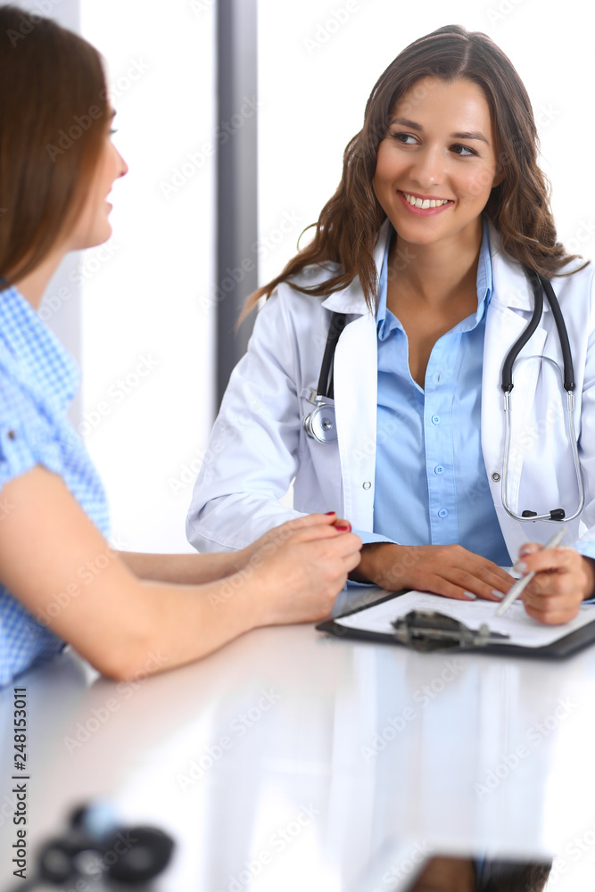 Doctor and happy patient talking while sitting at the desk. The physician or therapist discussing healthy lifestyle. Health care, medicine and patient service concept Doctor and happy patient talking while sitting at the desk. The physician or therapist discussing healthy lifestyle. Health care, medicine and patient service concept