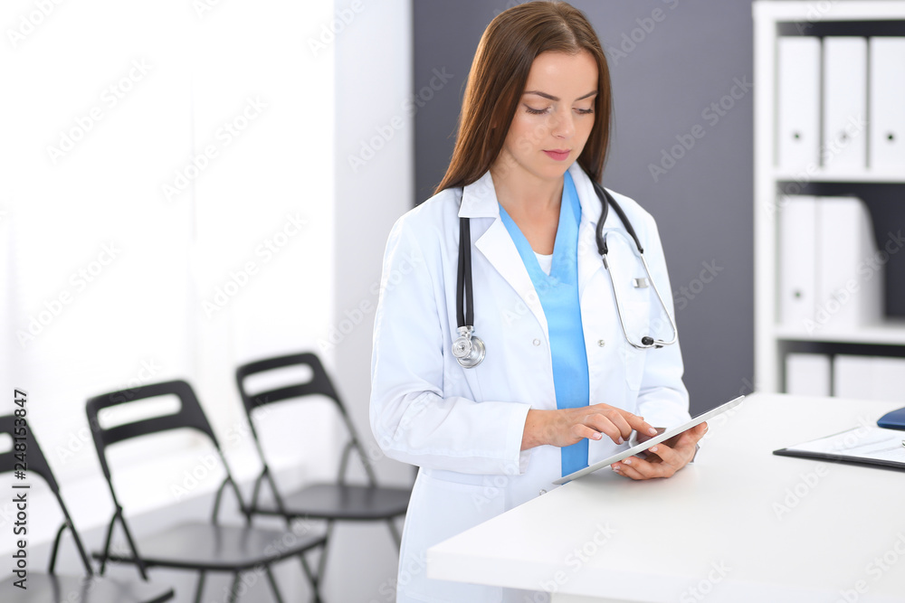 Doctor woman at work. Portrait of female physician using digital tablet while standing near reception desk at clinic or emergency hospital. Medicine and healthcare concept Doctor woman at work. Portrait of female physician using digital tablet while standing near reception desk at clinic or emergency hospital. Medicine and healthcare concept