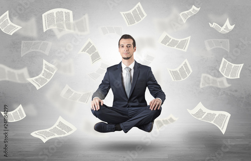 Young businessman meditating with documents and papers flying around him

