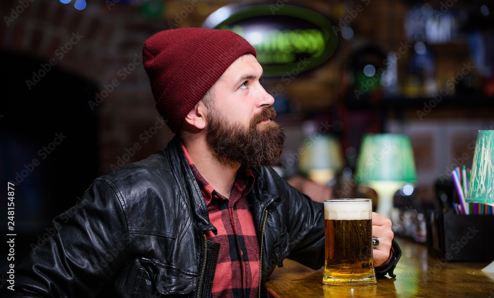 Hipster relaxing at pub. Man with beard spend leisure in dark pub. Brutal hipster relaxing. Guy bearded man sit at bar counter in pub. Weekend lifestyle. Pub great place to dine drink and have fun