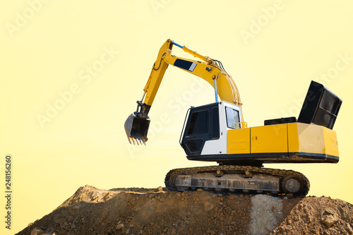 Industrial excavator working on construction site to clear the land of sand and soil at sunset photo