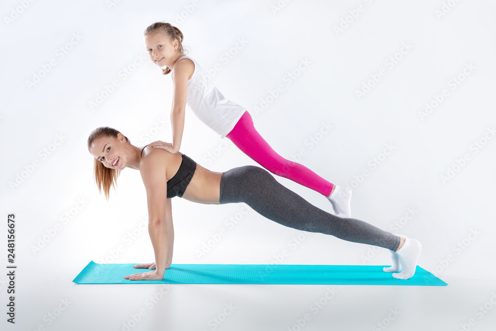 Beautiful woman and her little daughter are doing exercises on mats