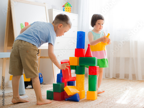 Happy preschool children play with toy blocks. Creative kindergarten children build a castle of plastic cubes. Educational toys for the family. Brothers and sisters play together in the room.