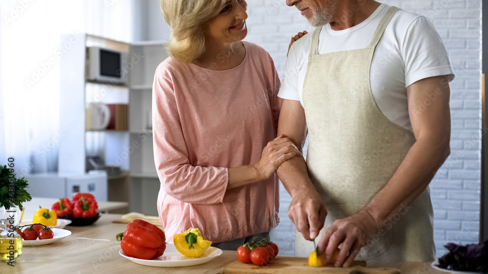 Caring husband in apron cutting fresh pepper for salad looking wife, relations Caring husband in apron cutting fresh pepper for salad looking wife, relations