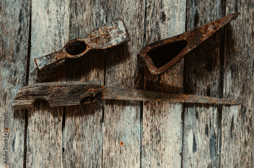 Old rusted hammer, cleaver and hacksaw with wooden handle on wooden background.