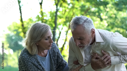 Old man having sudden heart attack during walk in park, wife helping him, care