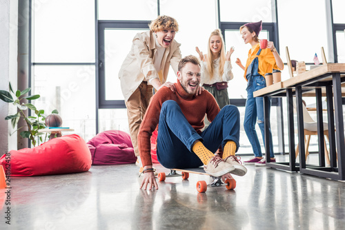 smiling casual business colleagues having fun and riding skateboard in loft office