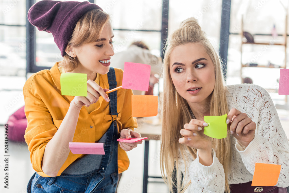 beautiful casual businesswomen putting colorful sticky notes on glass window in office beautiful casual businesswomen putting colorful sticky notes on glass window in office