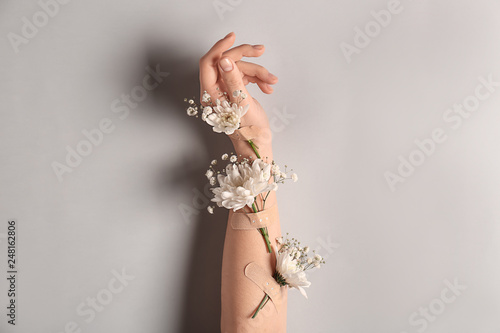 Female hand with beautiful flowers on light background