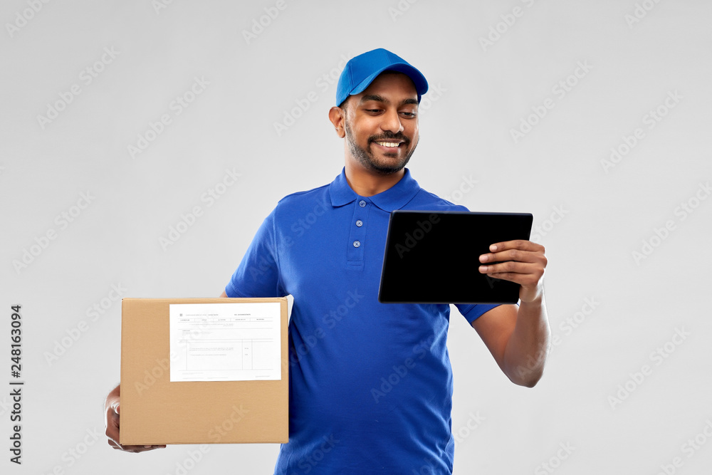 mail service, technology and shipment concept - happy indian delivery man with parcel box and tablet computer in blue uniform over grey background mail service, technology and shipment concept - happy indian delivery man with parcel box and tablet computer in blue uniform over grey background