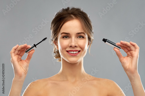 beauty, make up and cosmetics concept - smiling young woman with mascara over grey background