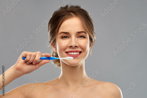 oral care  dental hygiene and people concept - smiling woman with toothbrush cleaning teeth over gray background