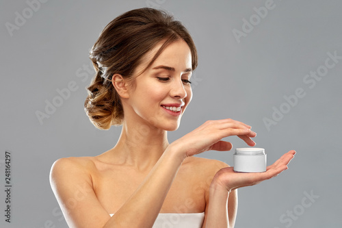 beauty, cosmetics and skincare concept - happy young woman holding jar of cream over grey background