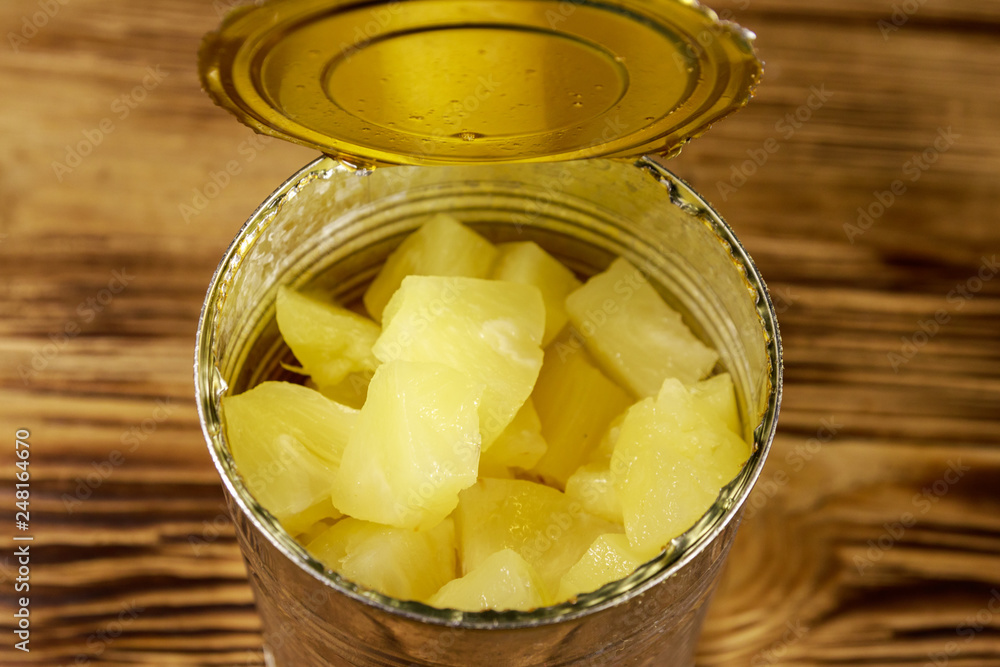 Opened tin can of pineapple pieces on wooden table Opened tin can of pineapple pieces on wooden table