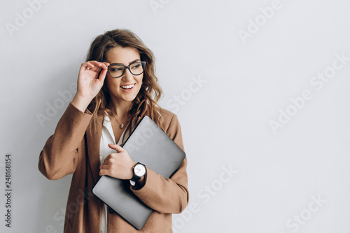 Beautiful business woman in a glasses with smile and a laptop in her hands in the office near a white wall with blank space for text photo