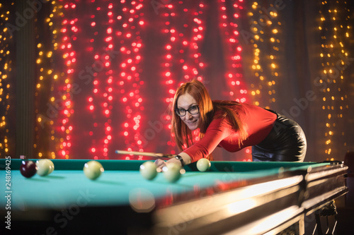 Smiling ginger woman playing billiard in nice architected club