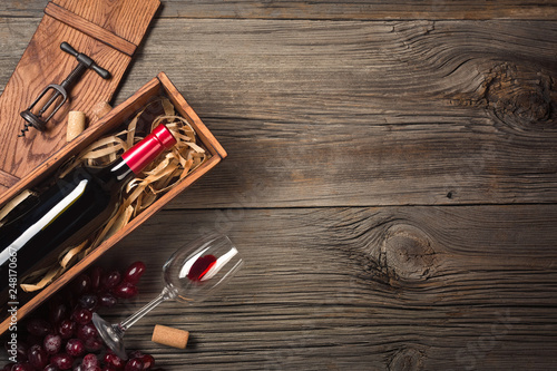 Red wine in a box with a glass and a corkscrew on a wooden table. Top view with space for your greetings.