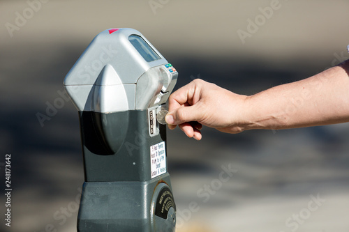 Adult's hand feeding quarters to a parking meter for extra time