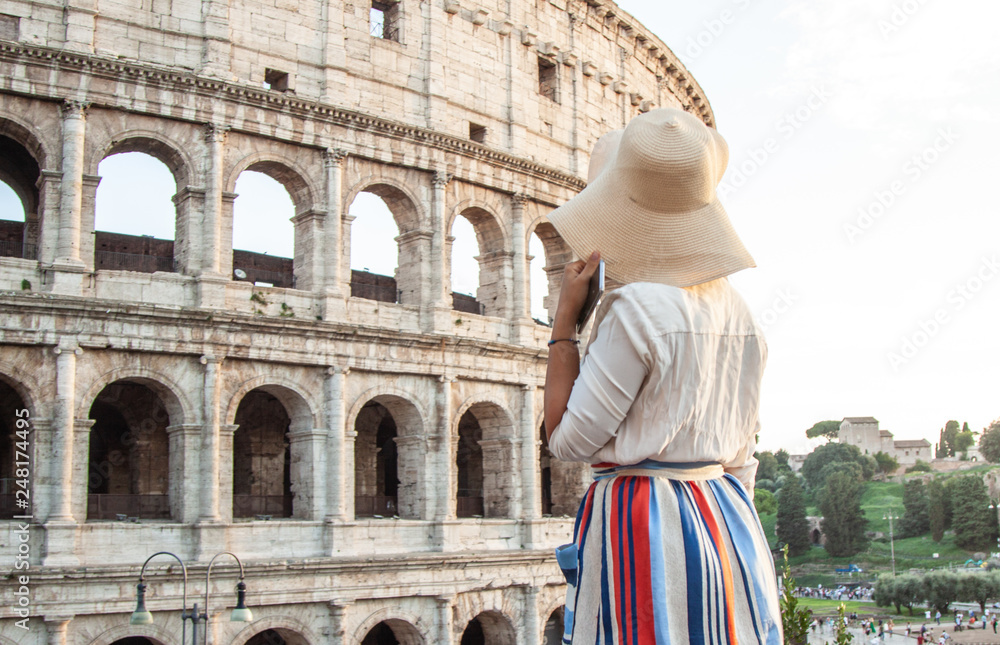 Beautiful young woman in fashion dress alone standing in front of colosseum in Rome at sunset.