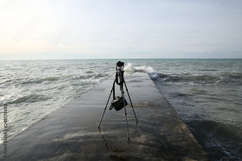 tripod with a camera is standing on the breakwater in the sea without a photographer