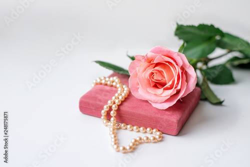 Pearl necklace on rose velvet box and pink one rose. Light background.