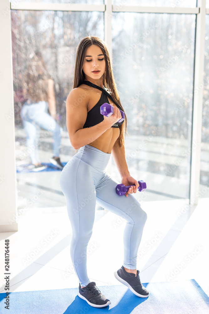 Beautiful sporty woman doing power fitness exercise at sport gym. Concentrated girl working out with dumbbells Beautiful sporty woman doing power fitness exercise at sport gym. Concentrated girl working out with dumbbells