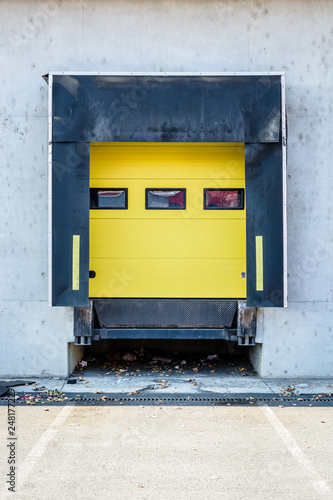 Front view of a truck loading bay with rubber seals in the concrete wall of a warehouse in the suburbs of Paris, France, with a closed yellow roller shutter door.