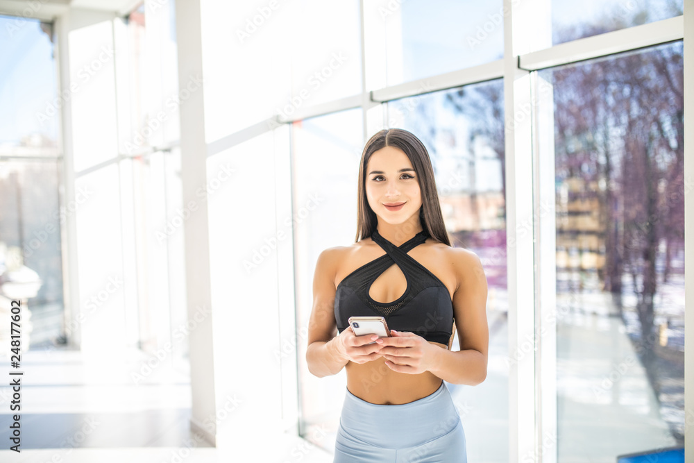 Portrait of personal trainer woman at gym after fitness workout and checking sport app in her smartphone.