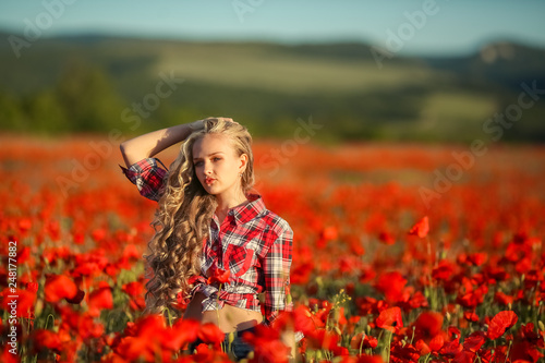 Young blonde in a red shirt in the poppy flower field.