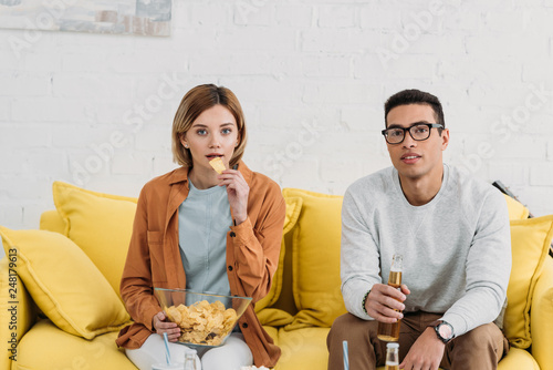 interracial couple enjoying snacks and drinks while sitting on yellow sofa photo