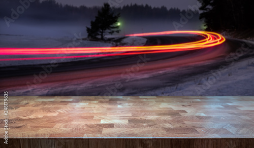 Empty table top for product display montage. Forest road with car tail lights blurred in the background.