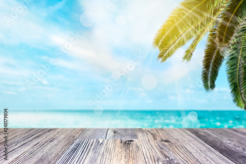 Empty wooden dock for product display montage. Tropical palm tree and ocean blurred in the background. Holiday concept. © Forenius