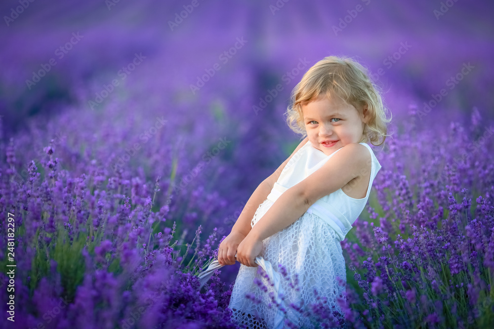 Cute curly young girl standing on a lavender field in white dress and hat with cute face and nice hair with lavender bouquet and smiling. Cute curly young girl standing on a lavender field in white dress and hat with cute face and nice hair with lavender bouquet and smiling.