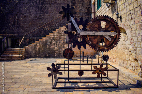 Vintage rusty clock mechanism consists of gearwheels, cogwheels,  clock hands in Medieval town Kotor, Montenegro. Brick wall in the background.  