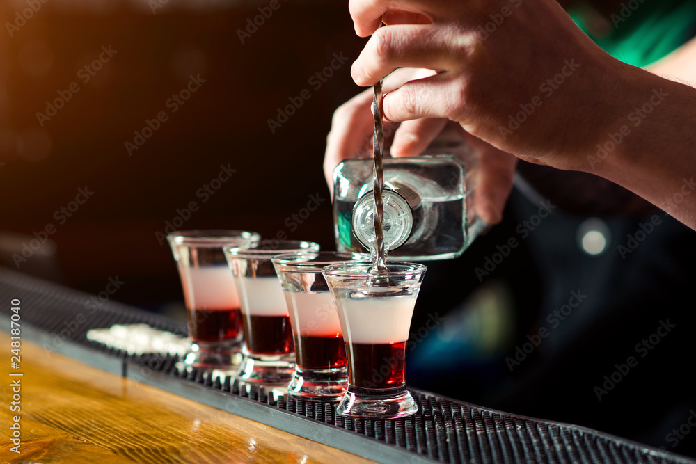 Barman make alcoholic shots in nightclub. Strong alcoholic drink. Multicolored shots on the bar. Small glasses with alcoholic drinks at bar counter. Party at nightclub.