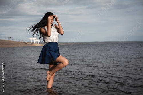 Brunette girl in a skirt standing in the water with her hair down. against the background of concrete and hydroelectric power. dramatic light.