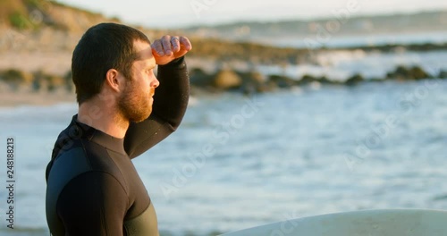 Side view of mid-adult caucasian male surfer with shielding eyes looking at sea at beach 4k