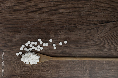 Wooden spoon filled with pills on wooden table